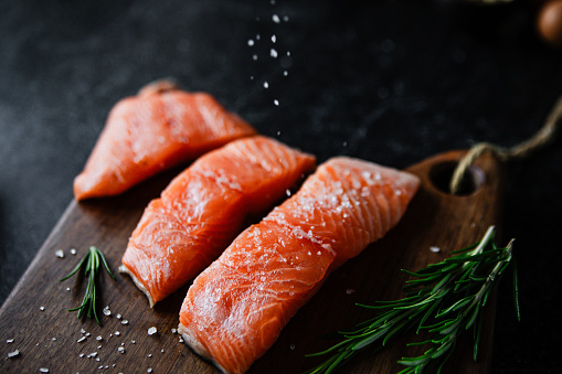 Close-up of raw salmon fillets with spices served on wooden board. Slices of salted salmon fish served with rosemary on wooden board.