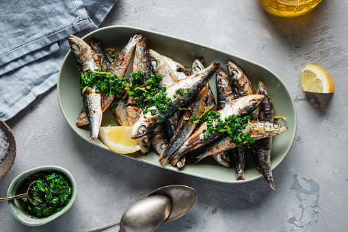 Homemade grilled fish with garlic, fresh parsley and lemon served on a plate. Delicious seafood served on dinner table.