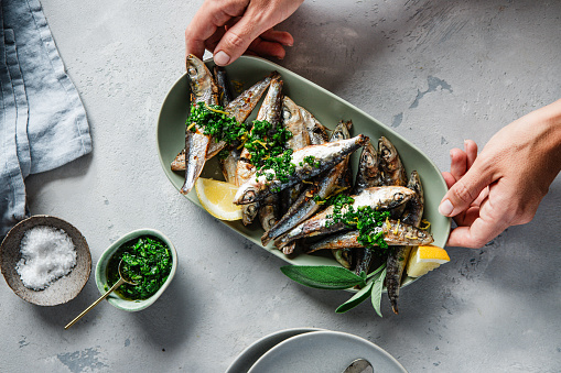 Female hands serving grilled sardines with spices on a table, Top view of a freshly baked fish on dining table.