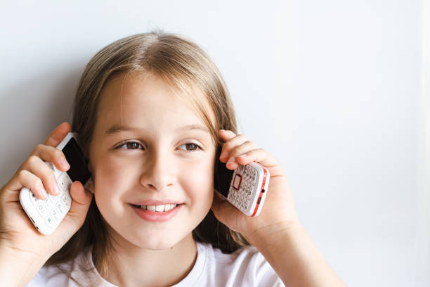 Cheerful girl is talking on two push-button phones on a light background