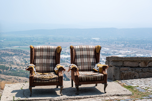 Dramatized front view of a pair of old armchairs standing side by side on a hill.