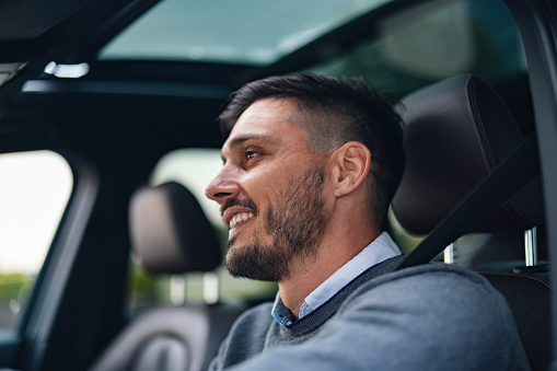A side view of a smiling Caucasian male driving his car.