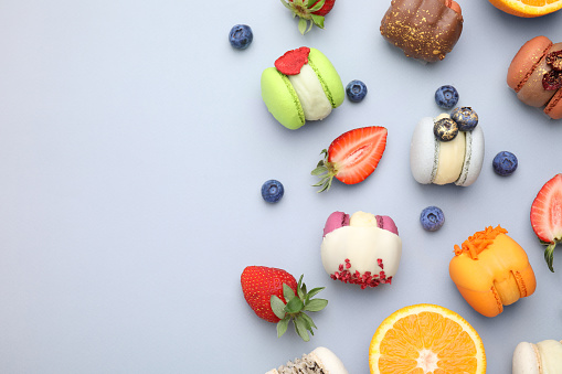 Delicious macarons, orange and berries on light blue table, flat lay. Space for text