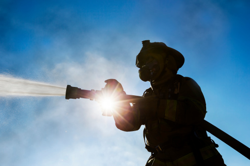 Fireman spraying fire photographed from low angle with the sun shining through. Horizontal shot.