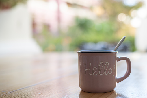 Cup of hot coffee on a wooden table outside the house with a message with the word Hello. Image with copy space. Life