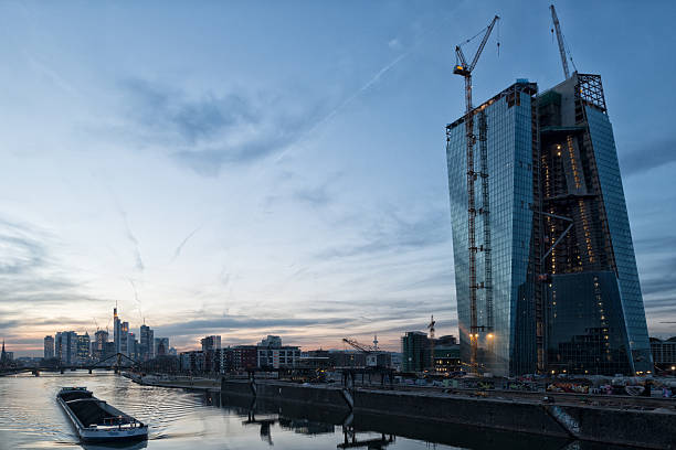 Frankfurt Skyline, Germany, Construction site of the European Central Bank at dusk. On the left side the skyline with the financial district of Ftankfurt. Blue toned picture with some noise. panoramic riverbank architecture construction site stock pictures, royalty-free photos & images