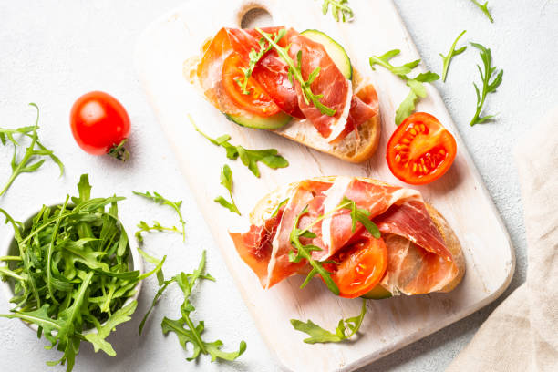 istock Open sandwiches with cream cheese, prosciutto, cucumber and arugula at white table. 1644794638
