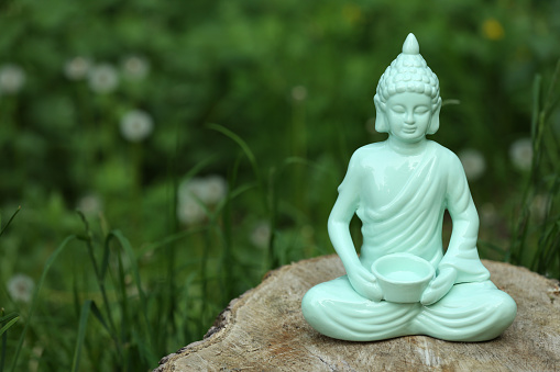 Decorative Buddha statue on stump outdoors, space for text