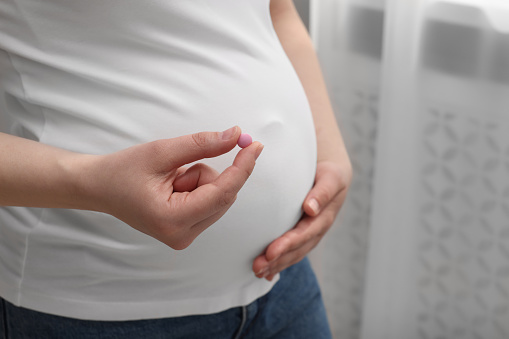 Pregnant woman with pill at home, closeup