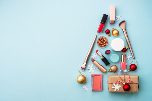 Christmas tree made from cosmetic and make up products on blue. Christmas sale and gift concept. Flat lay with copy space.