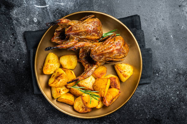 istock Delicious roasted quails with herbs in a plate with fried potato. Black background. Top view 1644903208