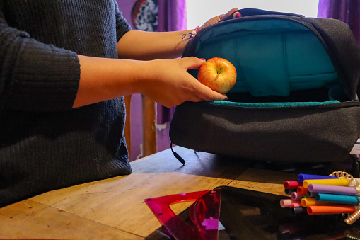 A woman puts an apple inside a backpack