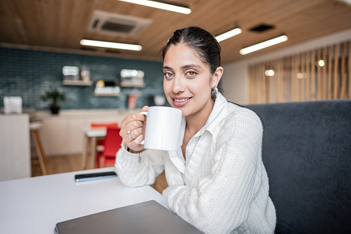Portrait of a young woman drinking coffee at office coffee shop