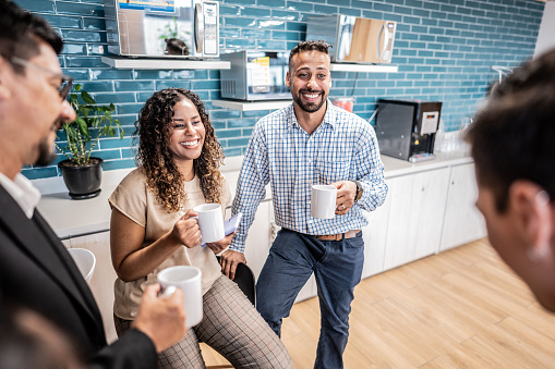 Happy coworkers talking while drinking coffee at office