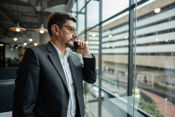 istock Mature man talking on phone while looking through window at office 1644942159