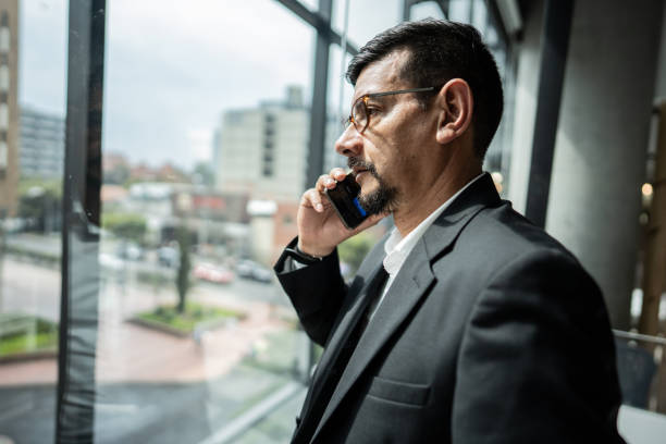 istock Mature man talking on phone while looking through window at office 1644942440