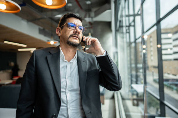 istock Mature man talking on phone while looking through window at office 1644942441