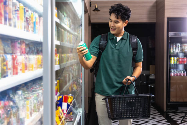 Happy Asian Young Man Shopping for Canned Beverages in Supermarket an Asian young adult man browses through the shelves of a well-stocked supermarket, searching for his favorite canned beverages. His happy demeanor reflects the ease of shopping grocery shelf cans stock pictures, royalty-free photos & images