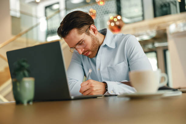 istock Handsome male freelancer making notes during working on laptop sitiing desk in coworking 1644961194