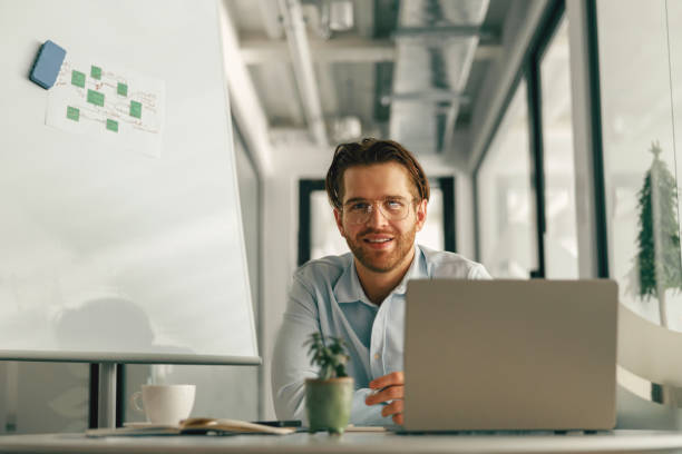 istock Smiling male manager drinking coffee during working on laptop in modern office and looking at camera 1644961219