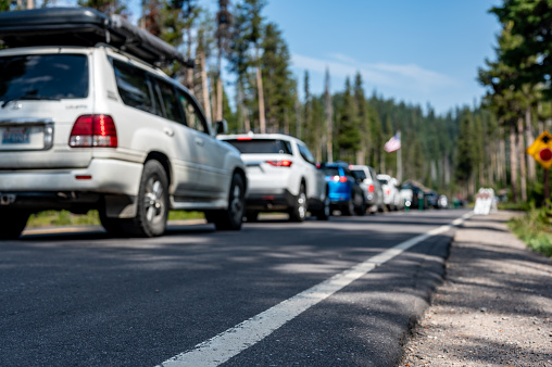 Selective focus on a paved road with a defocused long line of vehicles to enter a national park in the background. High quality photo