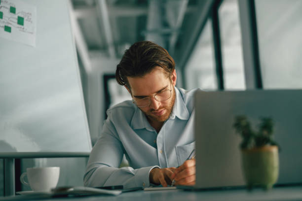 istock Focused male freelancer making notes during working on laptop sitiing desk in coworking 1644977634
