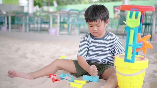 A little boy plays with toys in a sandpit alone.