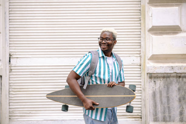 istock Handsome young African American man carrying longboard and walking 1644997895