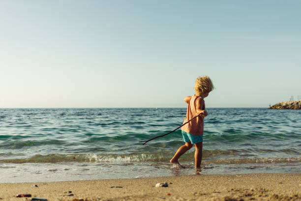 istock a little blond boy walks along the seashore with a stick in his hand plays laughs runs 1645007533