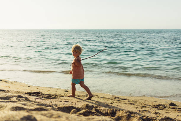 istock a little blond boy walks along the seashore with a stick in his hand plays laughs runs 1645012804