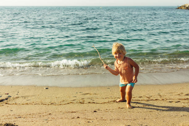 istock a little blond boy walks along the seashore with a stick in his hand plays laughs runs 1645014898