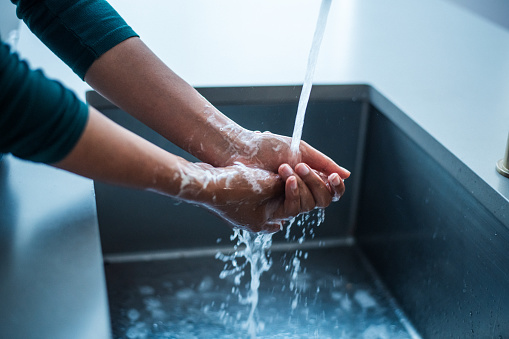 Cropped photo of an unrecognizable black woman washing her hands in a modern kitchen sink.