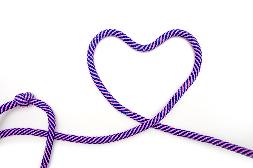 Multicolored rope with a heart shape on a white background. A blue-pink rope is twisted into a heart shape on a paper background. Love concept or wedding decor in minimalist style