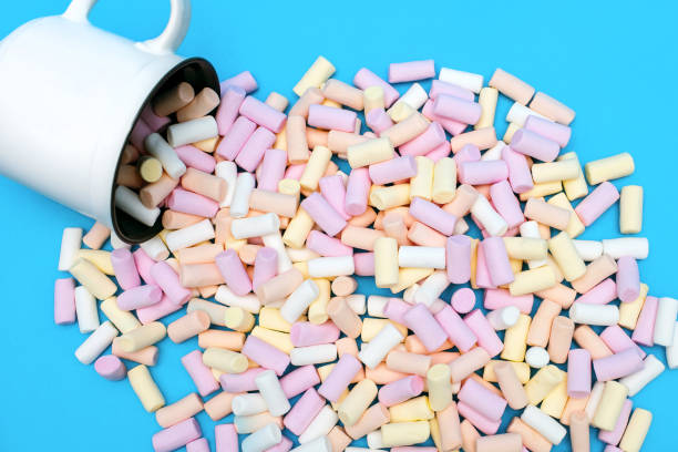 istock Multi-colored marshmallows are scattered next to a white mug on a blue background 1645131225