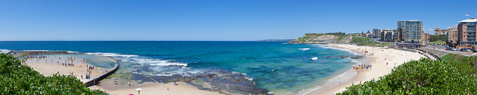 Wide angle view of Newcastle Beach and Canoe Pool in summer with the beach populated with beach goers.