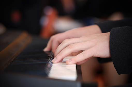 Close up of hands and fingers playing a keyboard or piano white keys. Audience blurred in background.  Left hand in focus