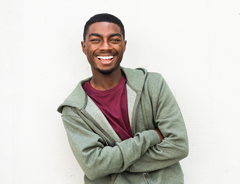 Portrait handsome young black man smiling with arms crossed by white background