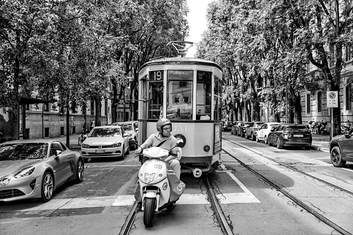 Milan, Italy - July 12, 2022: A motor scooter rider in front of a street car at a stop light in the streets in Milan