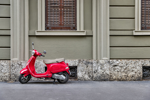 Milan, Italy - July 12, 2022: A classic red motor scooter parked in front of a building on the streets of Milan