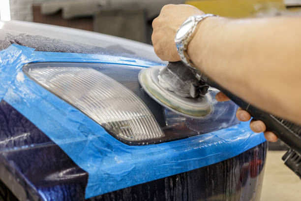 istock Man making headlight clean with polishing machine selective focus. Close-up. Master repairman polishing headlights of car in workshop using machine closeup. 1645312935