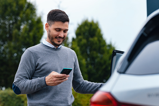A smiling Caucasian male using his smartphone after driving his vehicle.