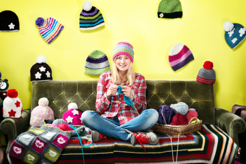 Young woman knitter portrait on couch with winter hats