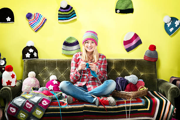 young woman knitter portrait on couch with winter hats - relaxation working humor sofa - fotografias e filmes do acervo