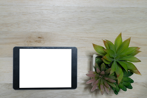 Black tablet on the wood table background with flower pot with copy space.