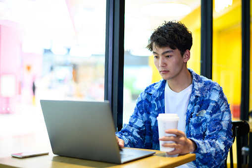 Asian young man using laptop in coffee shop