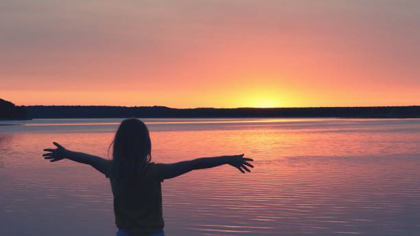 istock Girl with Open Arms Facing Lakeside Sunrise 1645537901
