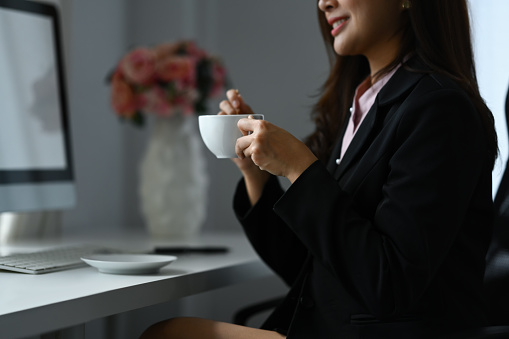 Dreamy businesswoman holding coffee cup, looking away, taking break at workplace, planning vision and strategy.