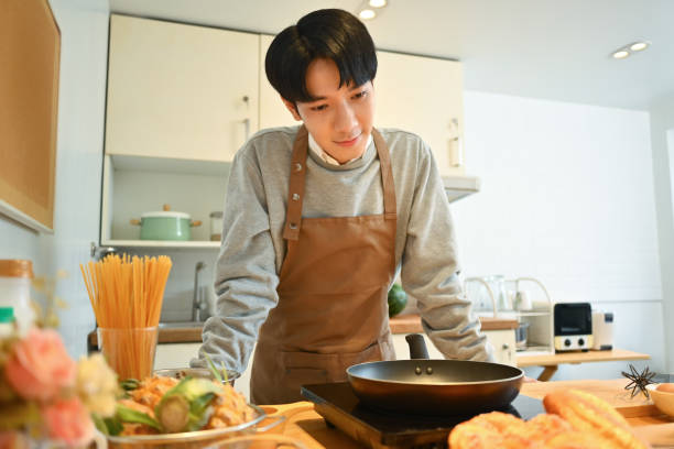 istock Handsome asian man in apron preparing breakfast in kitchen, making pancakes on frying pan 1645568523
