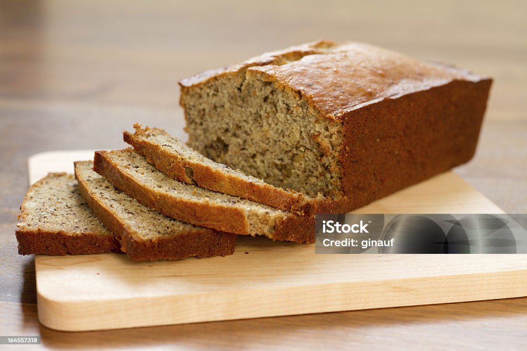 Banana nut bread - plain a photo of freshly baked and sliced banana nut bread on a wooden cutting board.  the loaf is made with both all purpose and whole wheat flours, salt, baking soda and powder, butter, sugar, eggs, mashed bananas, vanilla, and nuts. Banana Bread Stock Photo