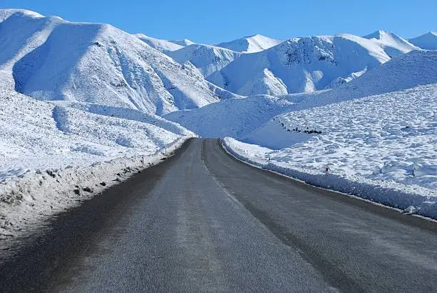 A road, the Great Alpine Highway, leads through the snow into the beginning of the Southern Alps, New Zealand.